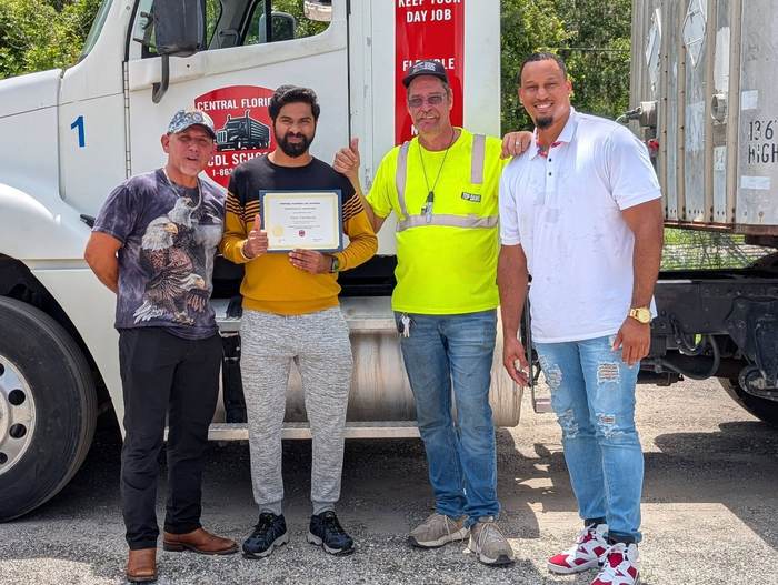 Central Florida CDL School graduate Tijo Thomas holding his certificate of completion with instructors