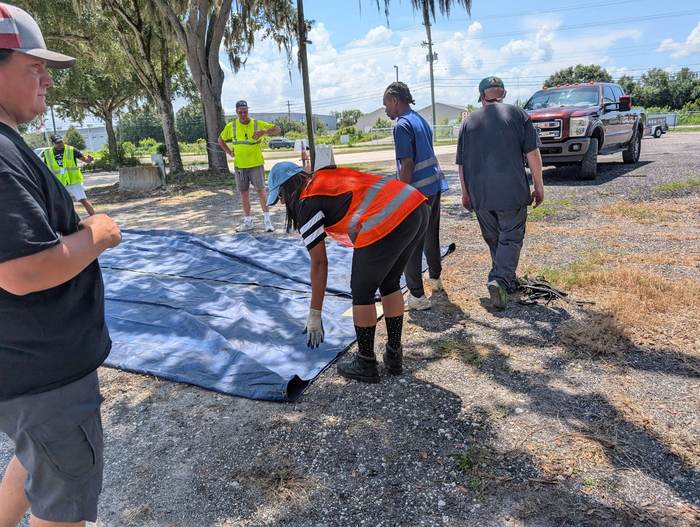 A student inspecting a curtain-side trailer tarp laid out on the ground during training