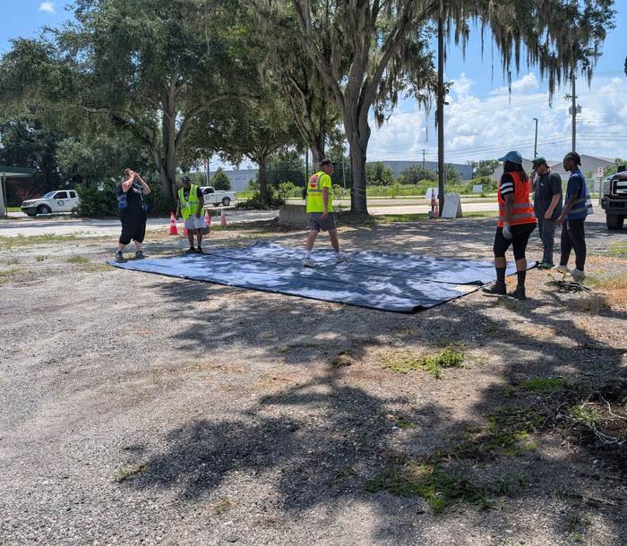 Students and an instructor working together to lay out a large curtain-side trailer tarp