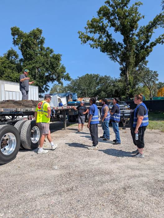 An instructor demonstrating chain and binder load securement on a flatbed trailer to a group of students