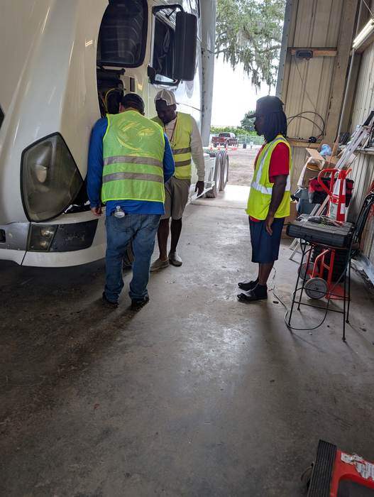 Prospective students and an instructor looking inside a truck's engine bay during a free session