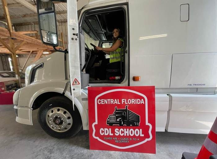 A woman CDL student sitting in the driver's seat of a training truck